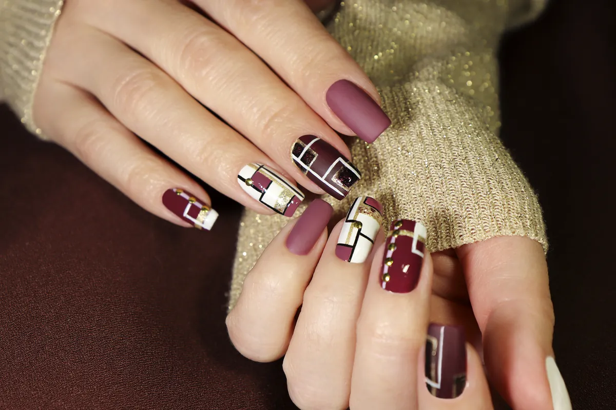 Nägel in Bordeaux, Mauve und Weiß mit geometrischer Nail Art vor beigem Strick