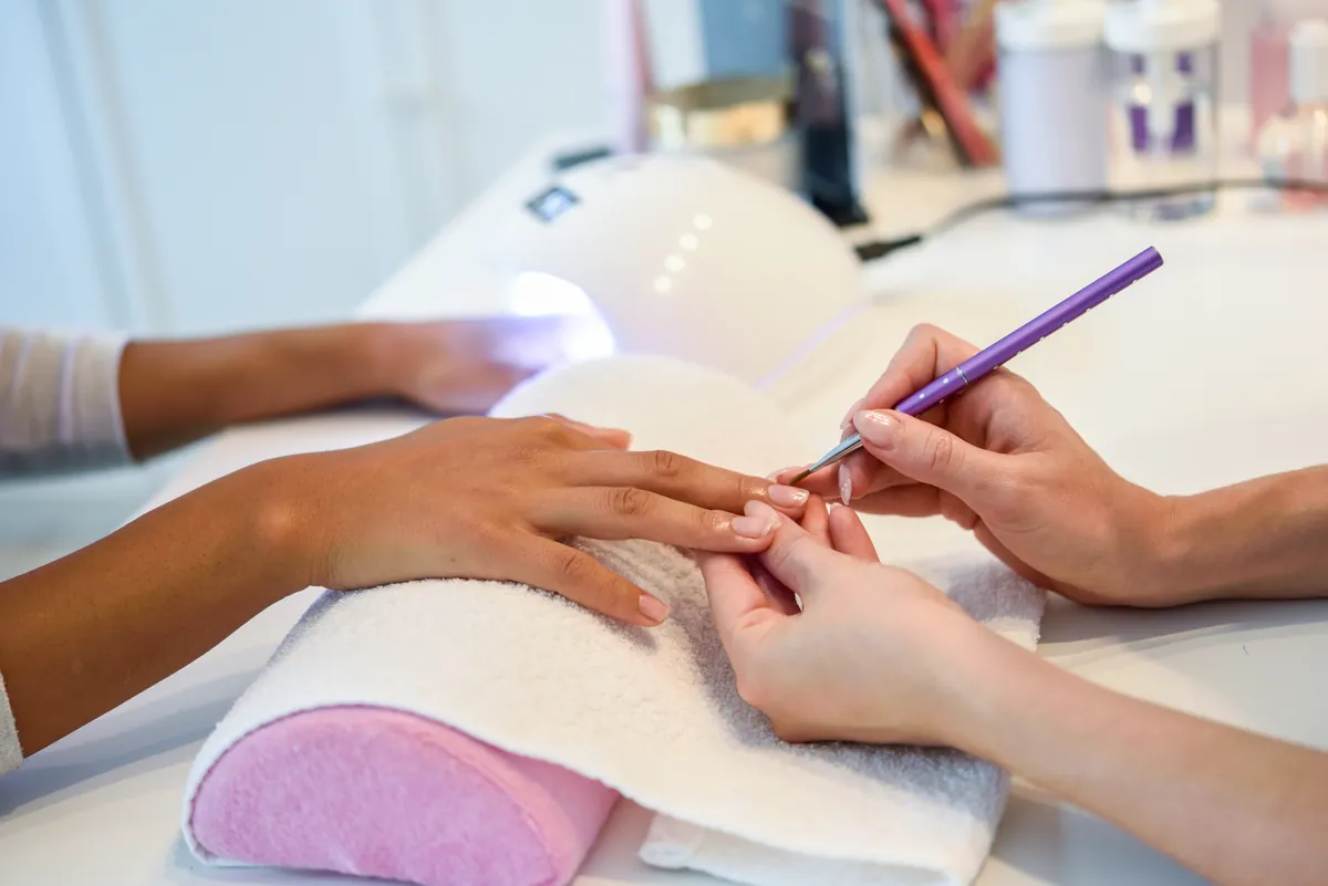 Eine Nageldesignerin trägt Gel-Lack neben einer LED-Nagellampe im Studio auf