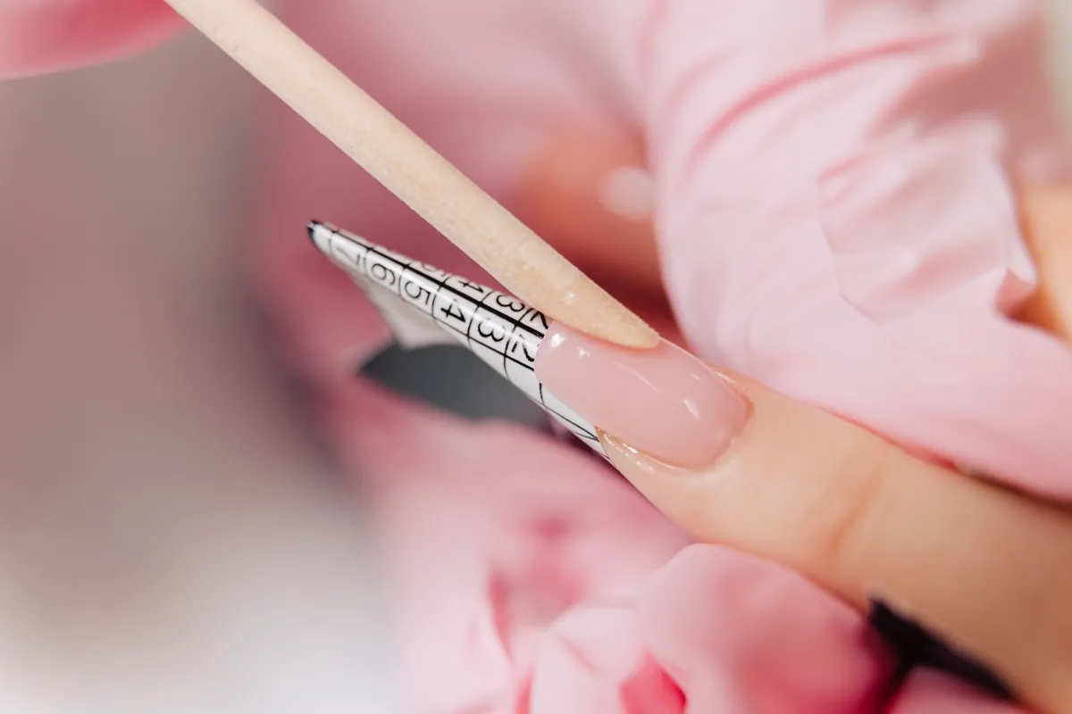 Eine Nageldesignerin formt eine Gel-Verlängerung mit einem Holzstäbchen