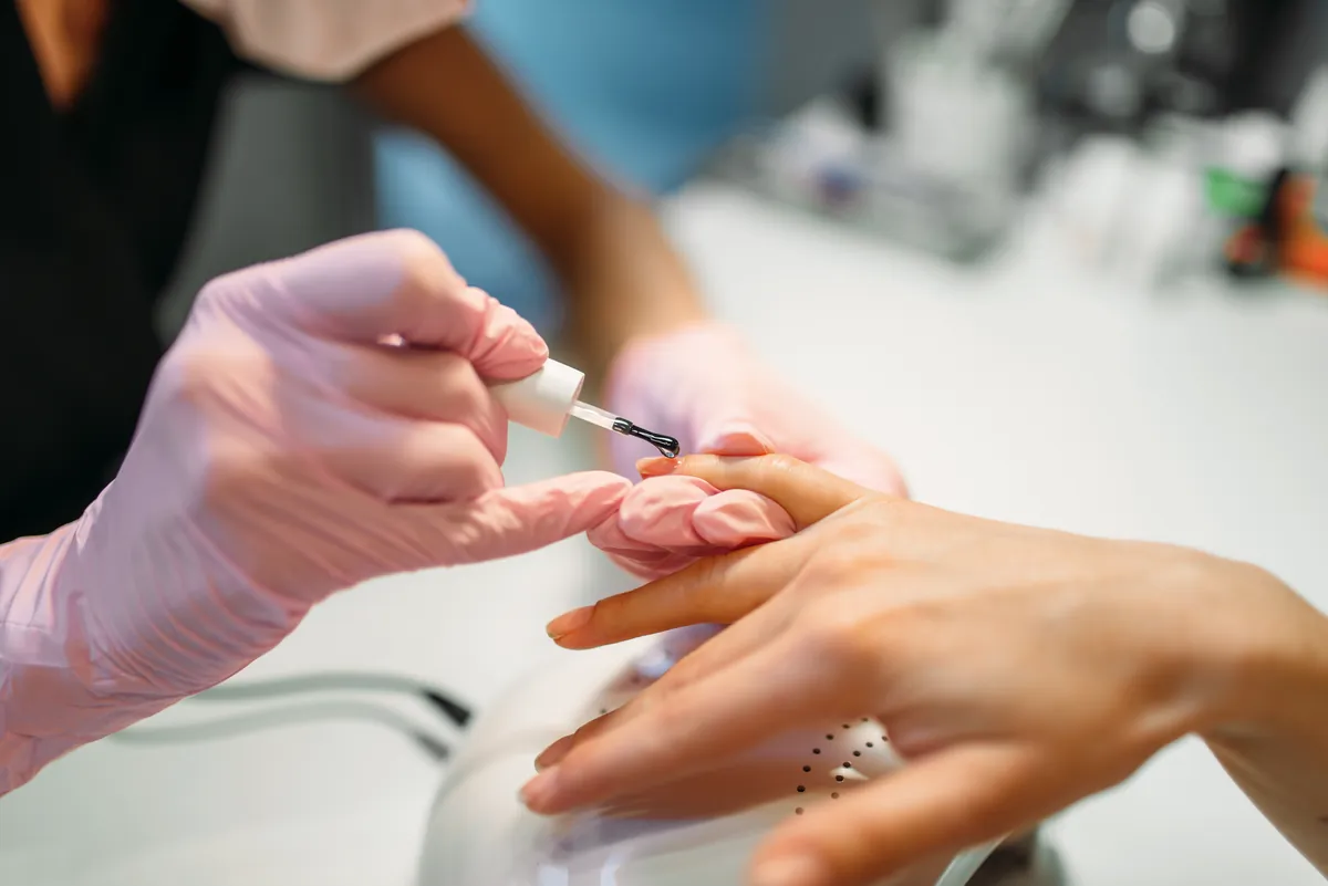 Eine Nageldesignerin mit Handschuhen lackiert die Nägel einer Kundin am Studiotisch