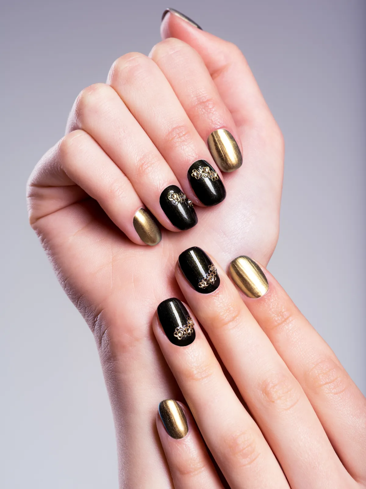 Kurze Nägel in glänzendem Schwarz und metallischem Gold mit feinen goldenen Ornamenten