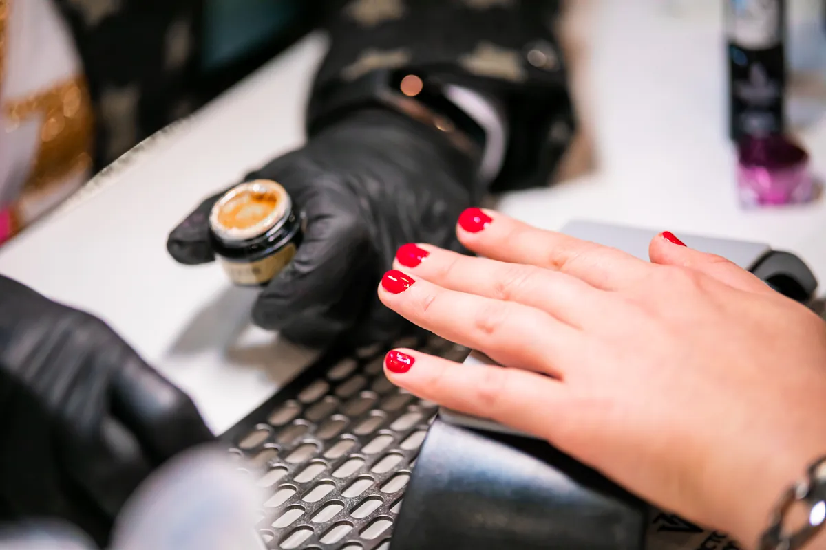 Eine Nageldesignerin mit schwarzen Handschuhen arbeitet im Studio an einer roten Maniküre
